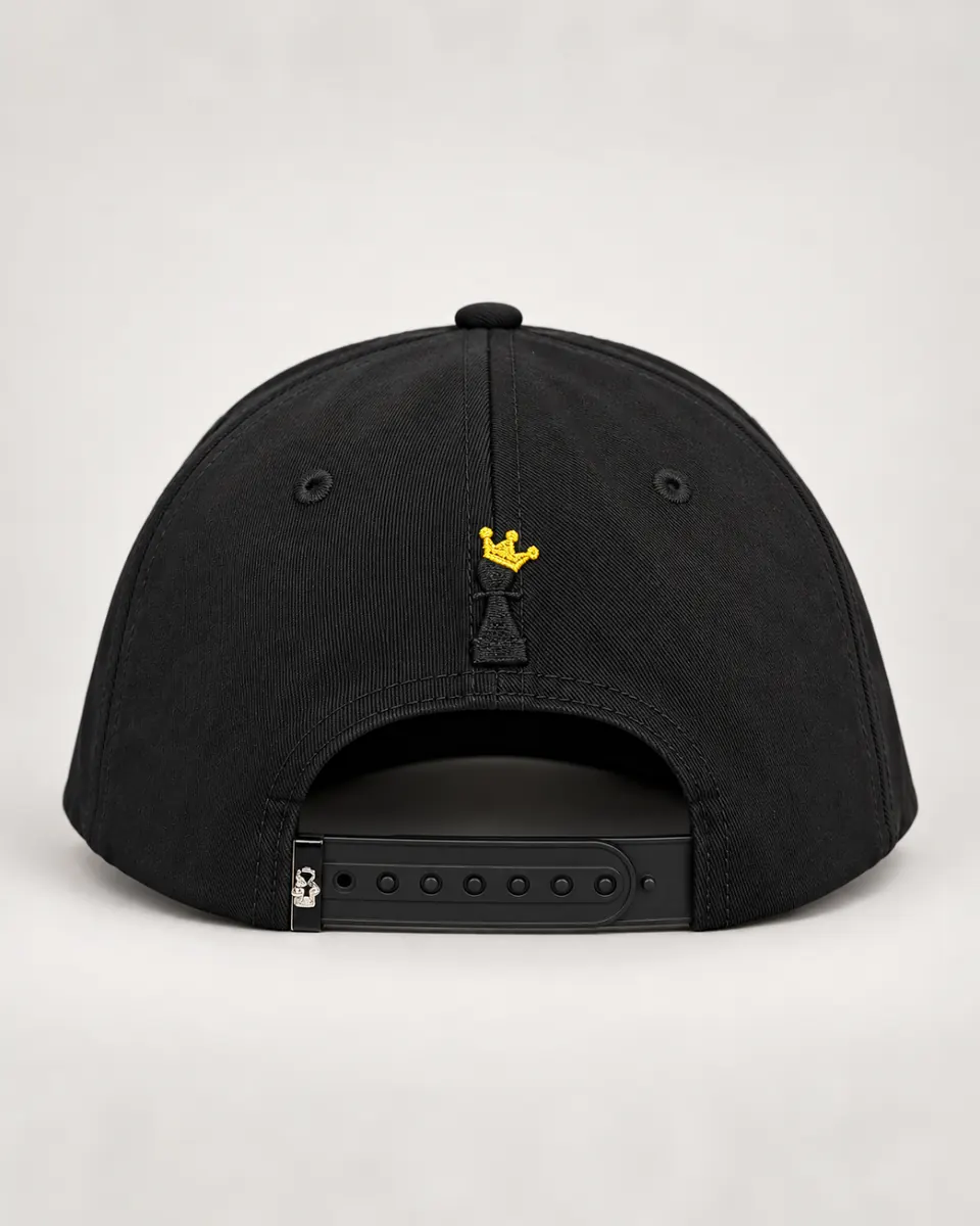 La parte de atrás de la gorra negra: una corona dorada bordada sobre un peón de ajedrez negro, y el cierre snapback